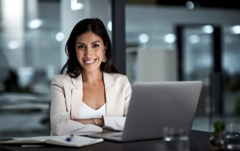 An image of a woman in a white shirt smiling while using a laptop Alt Text: Concept image for Sending a PDF File from Google Drive